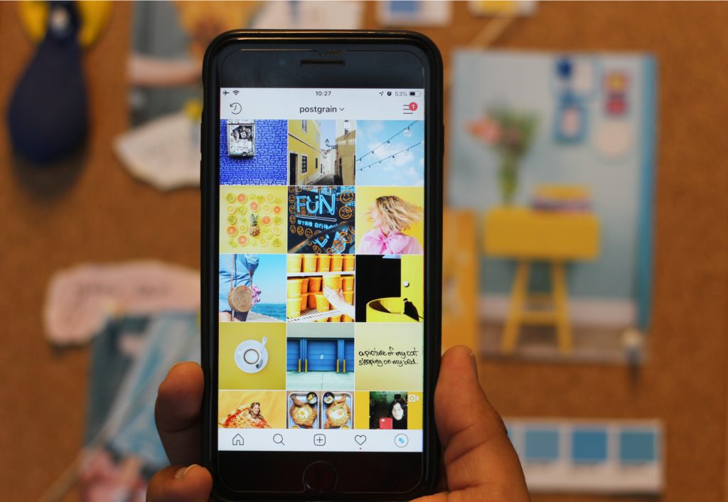 Celular aberto no perfil do Instagram do Postgrain com o feed organizado em fotos amarelas e azuis