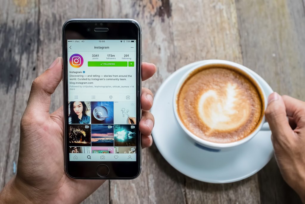 Homem segura um celular aberto no Instagram com a mão esquerda e, com a mão direita, segura uma xícara de café