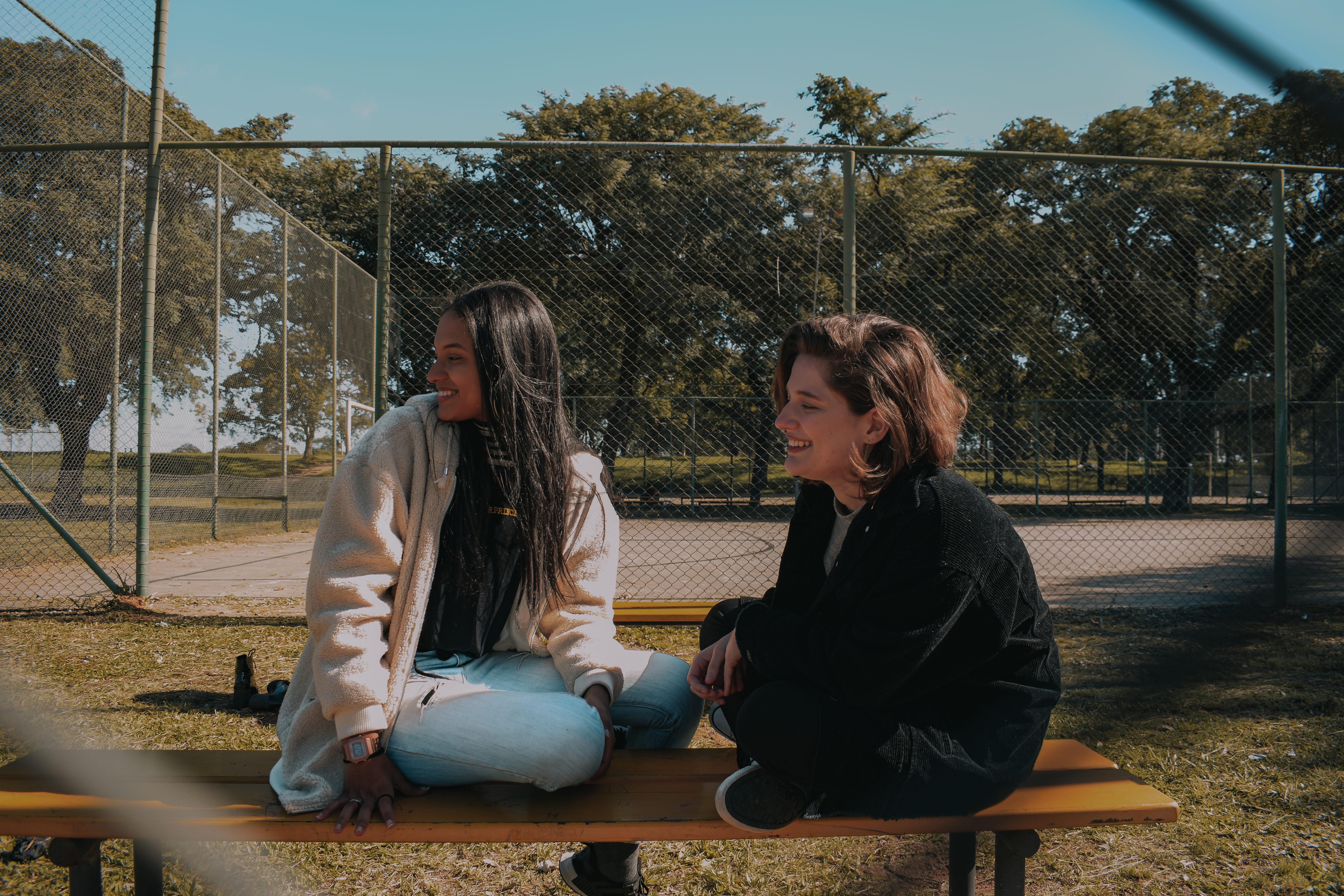 Mulheres LGBTs riem sentadas num banco de um parque