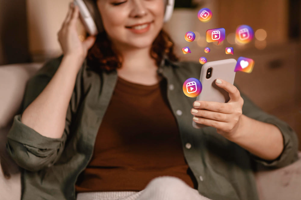 Mulher com headphone com celular na mão vendo como baixar Reels do Instagram