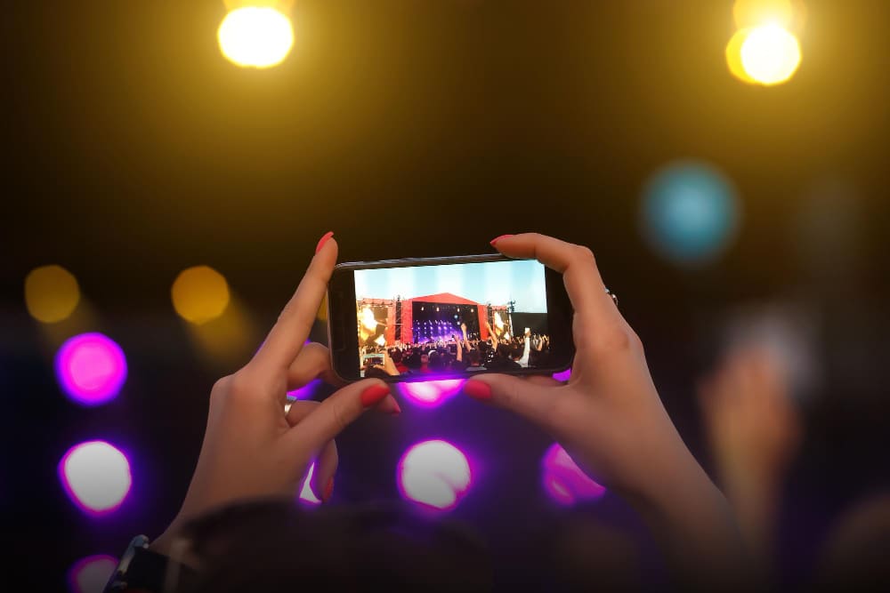 Eventos de social media em 2024 - Mãos segurando o celular tirando a foto de um palco num evento.