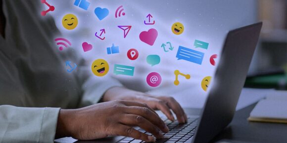 personalização no marketing digital - imagem de uma mão mexendo num computador e, dele, está saindo ícones de emojis.