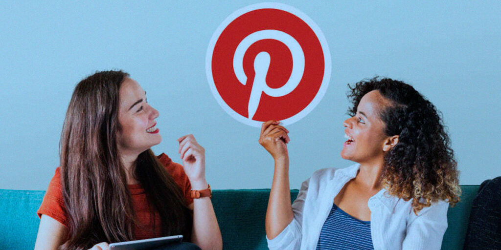 Pinterest Academy - A imagem que ilustra o tema tem duas meninas sentadas no sofá de uma sala. Uma é branca, de cabelo liso castanho, está usando camisa vermelha e calça jeans. A outra, está segurando a logo do pinterest, é negra, cabelos cacheados, tá usando calça jeans, camisa cinza e uma blusa de botão branca por cima. Ambas as meninas estão olhando para a logo do Pinterest e sorrindo.