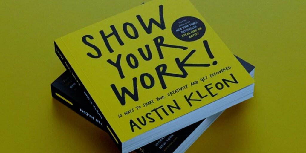 Melhores livros para social media - a imagem que ilustra o tema tem o fundo amarelo e no meio dois livros. O que aparece em destaque é o livro do Austin Kleon e o título dele é "Show Your Work".