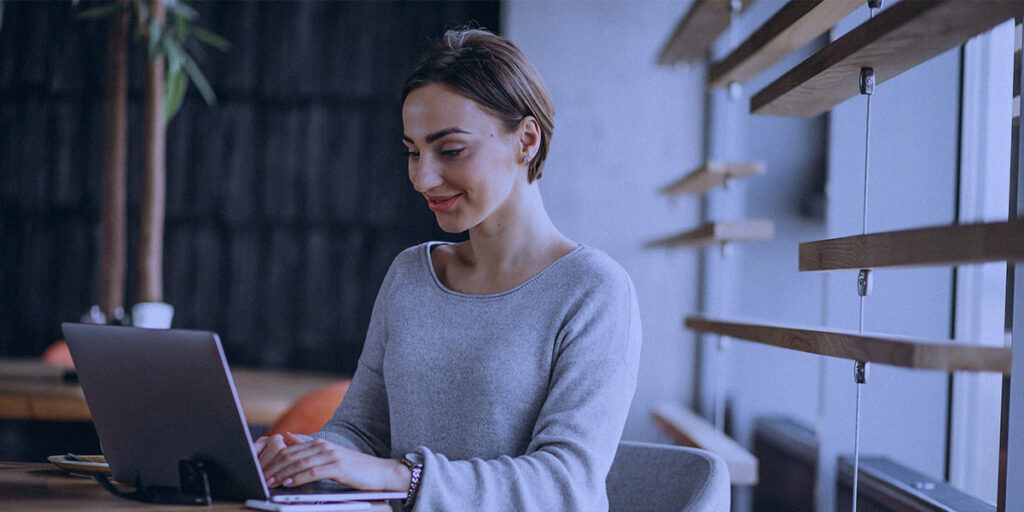 Plano de Marketing Digital - A imagem que ilustra o tema tem o fundo de uma sala de escritório onde aparece uma mulher sentada em frente uma mesa trabalhando.