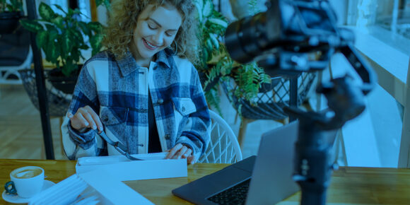 Mulher sentada com o notebook aberto, um café do lado e gravando um conteúdo de autoridade